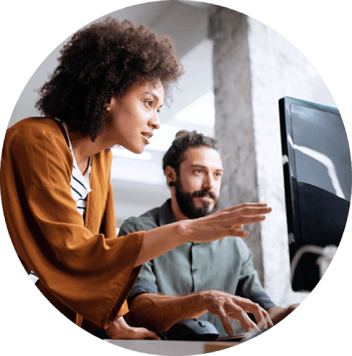 Two individuals working at a computer in an indoor setting, one pointing at the screen while the other observes